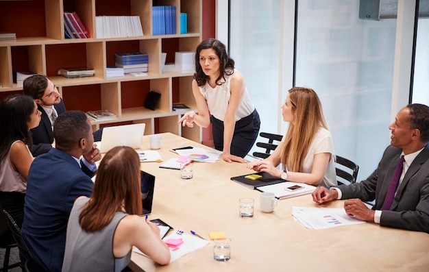 Female manager stands addressing team at boardroom meeting