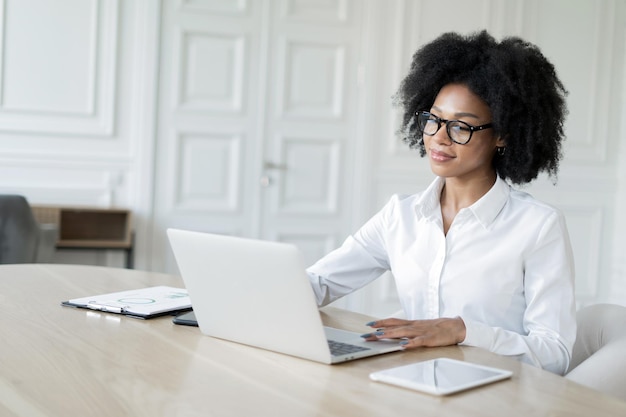 Женщина-менеджер в очках в формальной одежде работает в офисе, использует ноутбук