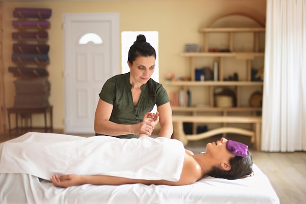 Female masseur giving massage to woman lying down and relaxing in therapy salon interior