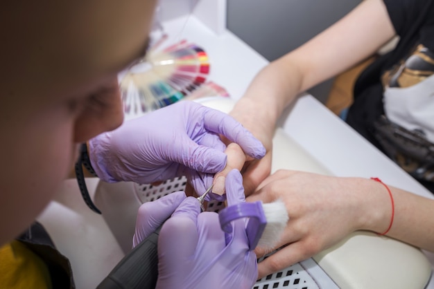 A female master uses an electric cuticle machine during a manicure at a salon. Hardware manicure close-up. Hand care concept.