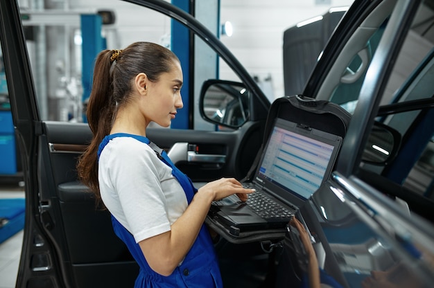 Female mechanic with laptop does the engine diagnostics, car service, professional inspection