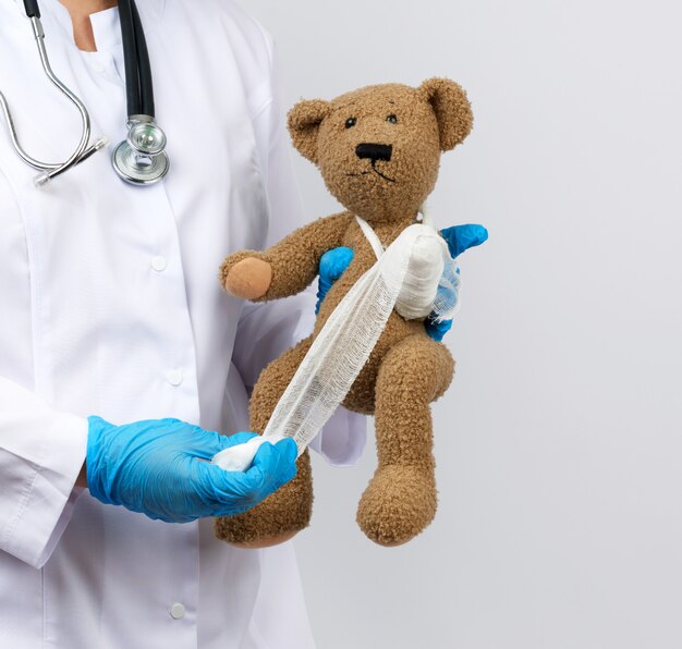 Female medic holds brown teddy bear and bandages paw with white gauze bandage