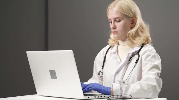 L'assistente medico femminile indossa camice bianco, videochiamata del paziente distante della cuffia avricolare sul computer portatile. medico che parla al cliente utilizzando l'app per computer di chat virtuale. telemedicina, concetto di servizi sanitari a distanza.