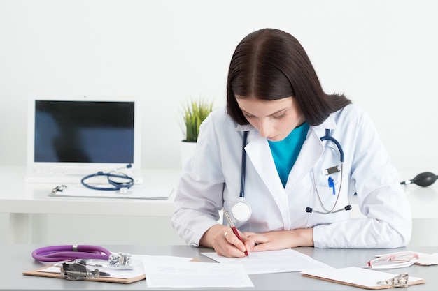 Female medical doctor writing something sitting at her office. Healthcare and medical concept.