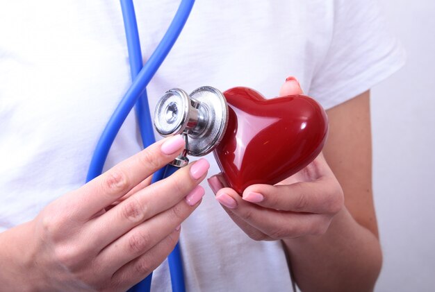 Доктор медицины женского пола держит в руках красное игрушечное сердце и голову стетоскопа
