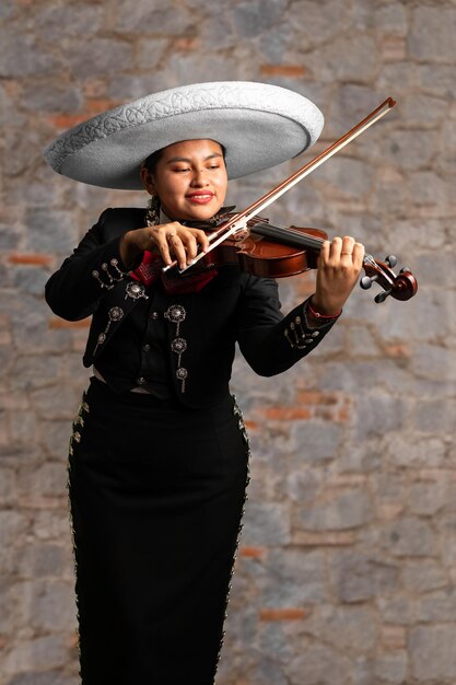 Female mexican mariachi woman playing violin traditional mariachi girl suit on a stone background