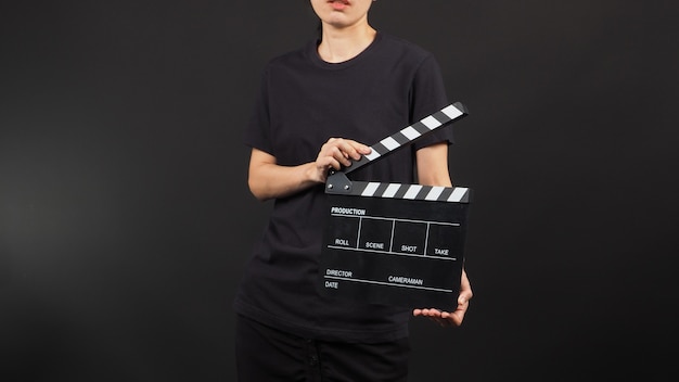 Female model holding clap board or movie slate use in video production and movie industry on black background.