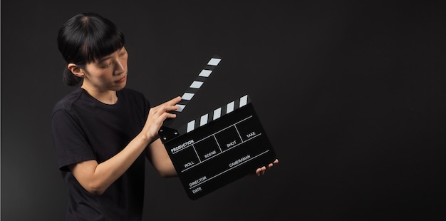 Modello femminile che tiene scheda applauso o uso di ardesia di film nella produzione di video e nell'industria cinematografica su sfondo nero.