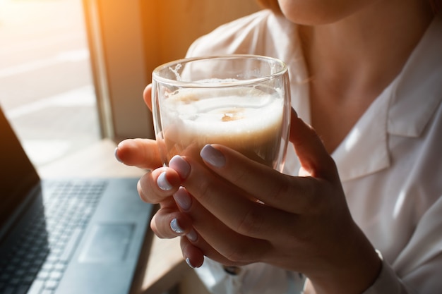 female model holds a cup of coffee in hand. close-up of coffee in hand