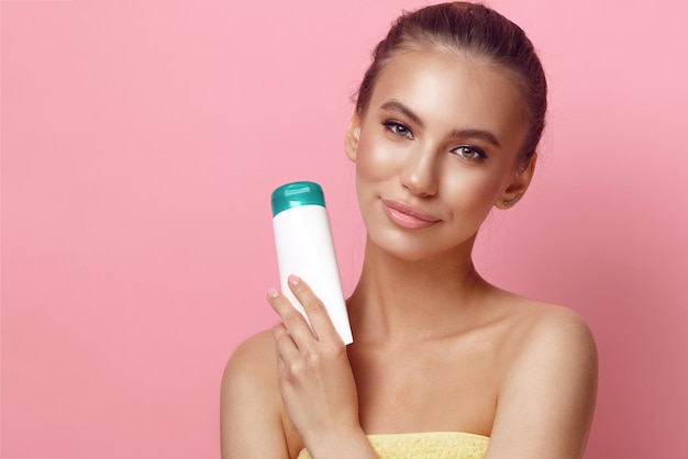 Female model holds plastic tube of lotion on pink background