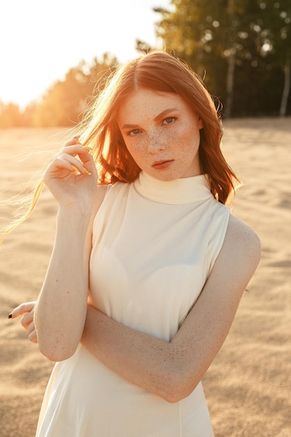 female model standing on sand dunes and touching long ginger hair