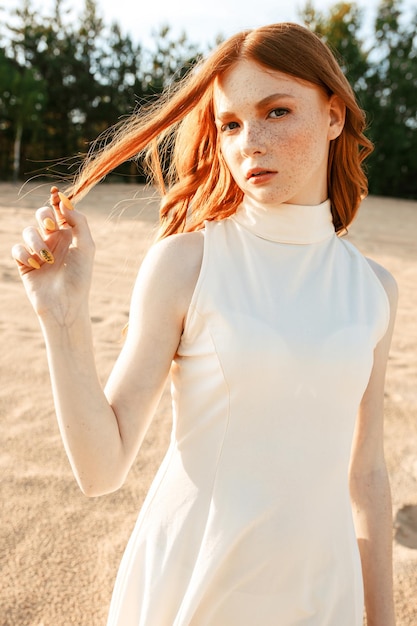 female model in stylish summer dress and with freckles standing on sand dunes