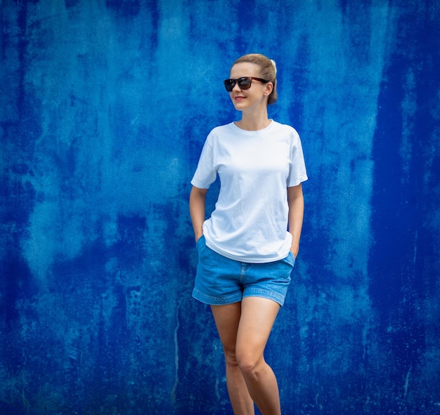 Female model wearing white blank tshirt on the background of an blue wall