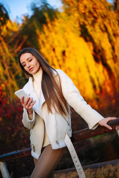 Female model with mobile outdoor Young pretty woman with phone on autumn park background