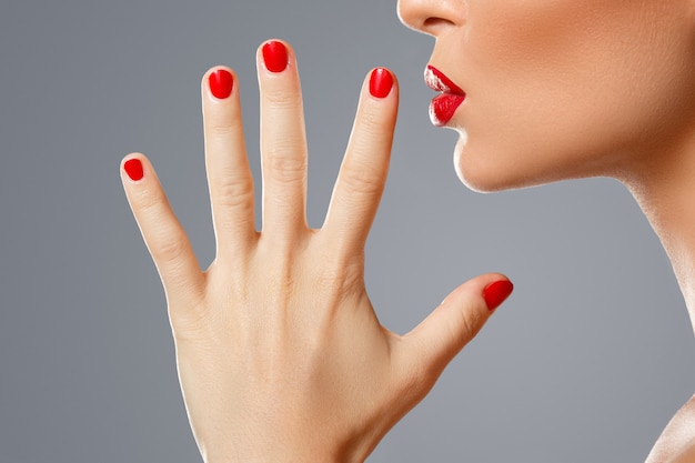 写真 女性の口と赤いマニキュアと口紅の爪。