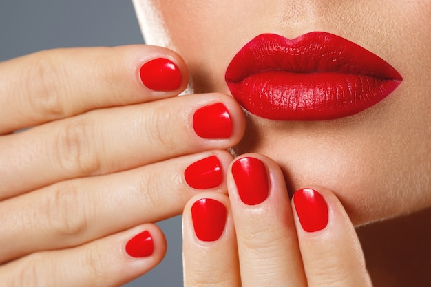 Foto bocca e unghie femminili con il manicure e il rossetto rossi.