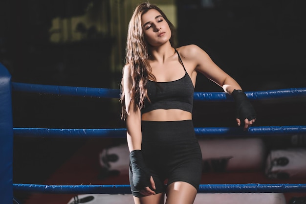 Female muay thai boxer resting after sparring on the ropes