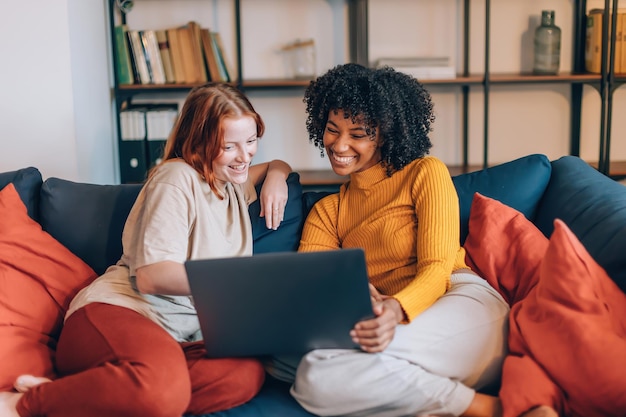 Female multiethnic friends on couch watching movie women flatmates surfing internet together