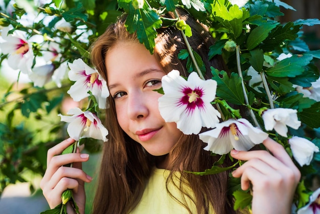 Female natural beauty cheerful pretty child at blooming tree outdoor vacation time summer fashion beauty beautiful teen girl with hibiscus bush flower kid spring fashion style happy childhood