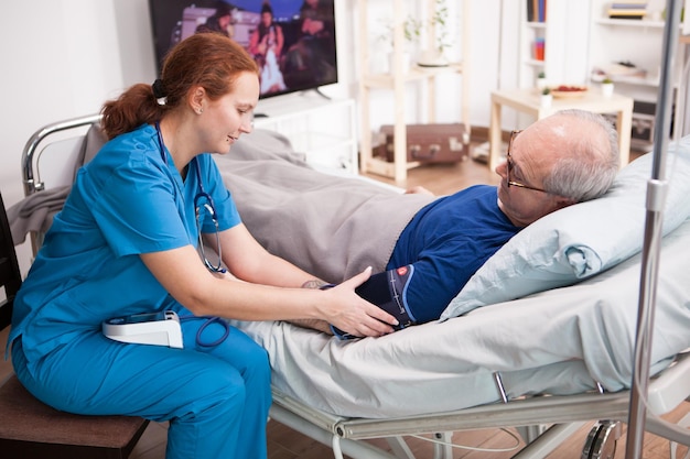 female nurse checking the blood pressure of retired man in nursing home.