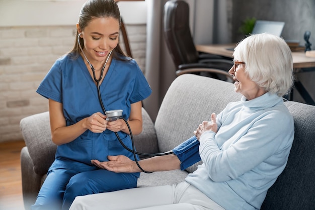집에서 노인 여성의 혈압을 확인하는 여성 간호사