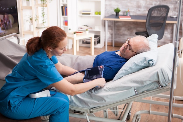 Женщина-медсестра проверяет артериальное давление у старика в доме престарелых.