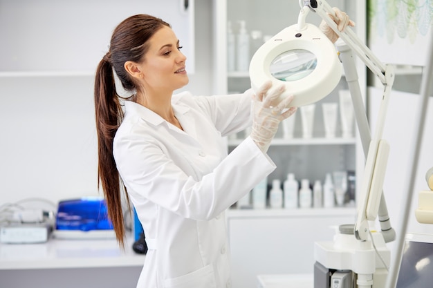 Female nurse fixing medical lamp in right position, preparing for work in the morning, at work place