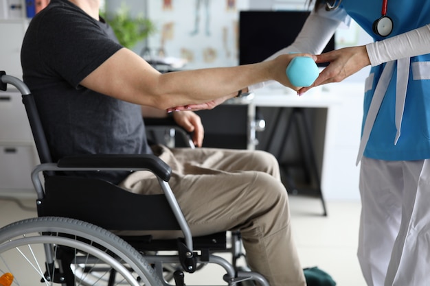 Female nurse helps lift dumbbell to disabled patient rehabilitation therapy