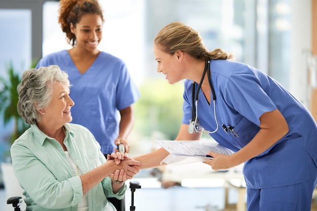 Женщина-медсестра держит медицинские записи, пожимая руку своему старшему пациенту в больнице