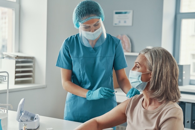 Female nurse making coronavirus vaccination to mature woman while working in the hospital