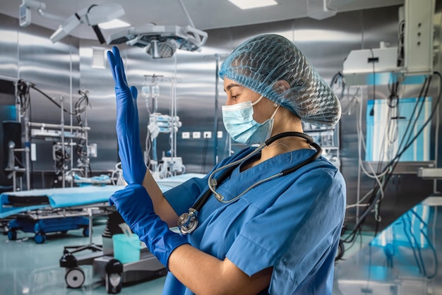 여성 간호사는 고무 라텍스 파란색 장갑을 끼고 복잡한 수술을 위해 마스크를 쓴 파란색 유니폼을 입습니다.