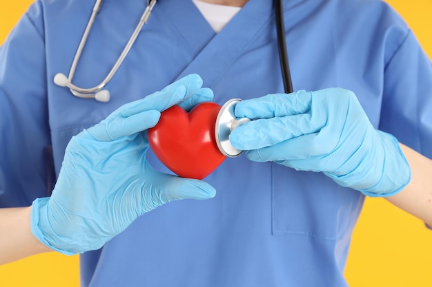 Female nurse with heart on yellow background, close up