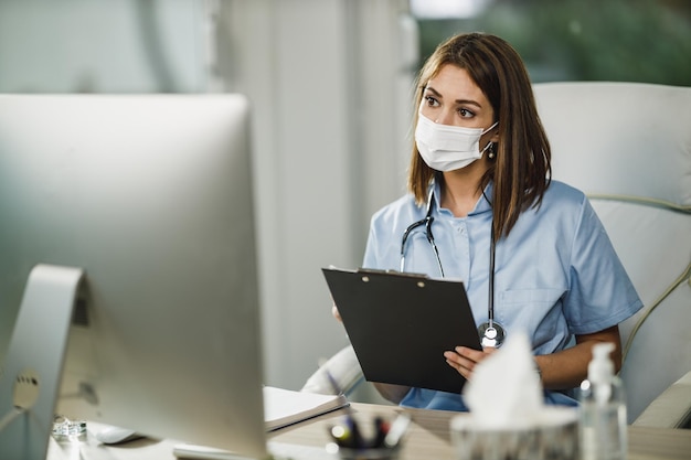 A female nurse with protective face mask having video call with patient on computer during corona virus pandemic.