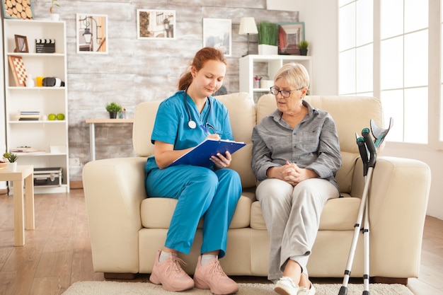 Photo female nurse writing on clipboard while talking with senior woman in nursing home.