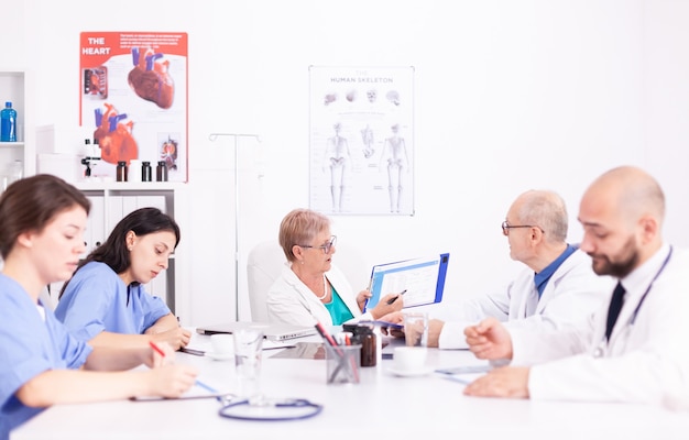 Female nurses taking notes while medical expert explaining about viral diseases in hospital conference room. Clinic expert therapist talking with colleagues about disease, medicine professional