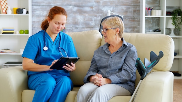 Female nuse helping senior elderly retired woman how to use her tablet computer in nursing home