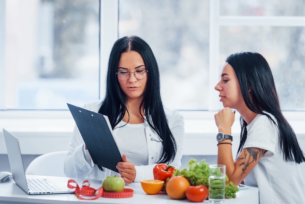 Female nutritionist gives consultation to patient indoors in the office by using notepad.