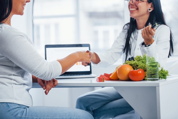 Female nutritionist gives handshake to patient indoors in the office.