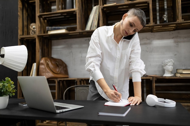 Female office worker speaks on the phone and makes notes in a notebook while standing near the