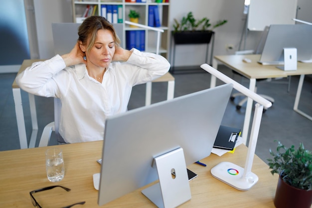 コンピューターで働きながらリラックスするためにストレッチする女性サラリーマン