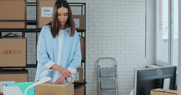 Female online store business owner worker packs books after ecommerce retail order delivery into box prepares package delivery on table