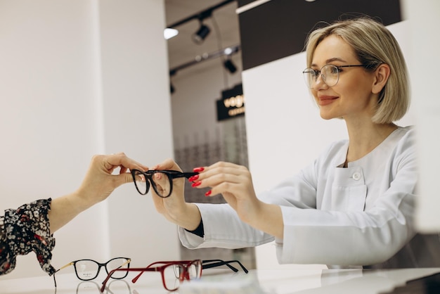 Female ophthalmologist at optical store helps to choose eyeglasses