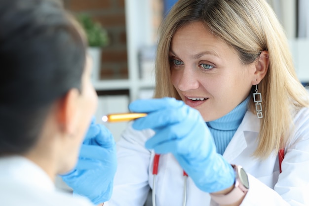 Female otolaryngologist doctor shines light down throat of patient with pain syndromes sickness