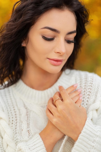 Female outdoors headshot portrait of beautiful young woman with clean beautiful face and skin with curly hair in vintage knitted sweater in autumn park Hand skin care