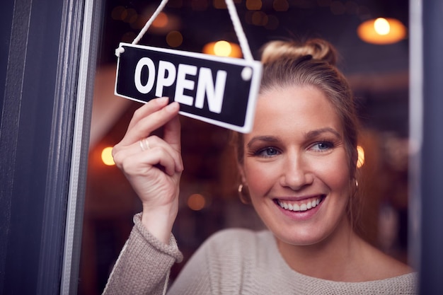 写真 店のドアに丸いオープンサインを回す中小企業の女性の所有者