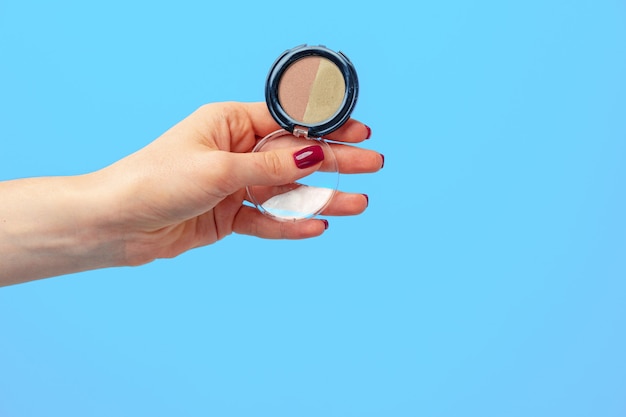 Female palm holding pack of eyeshadows against blue background close up