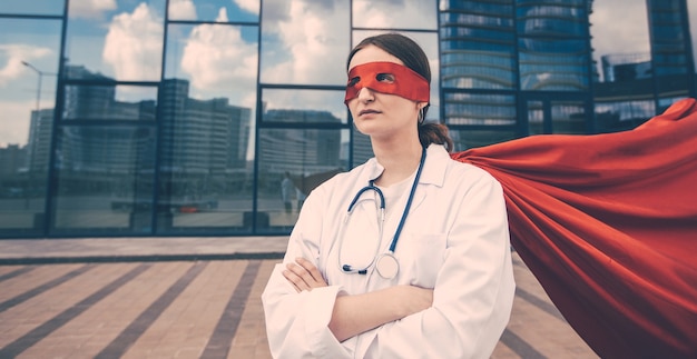 Foto paramedico femminile in un impermeabile da supereroe in piedi su una strada cittadina. foto con una copia-spazio.