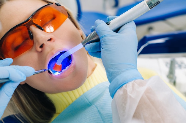 A female patient in dental glasses treats teeth at the dentist with ultraviolet light dental fillings