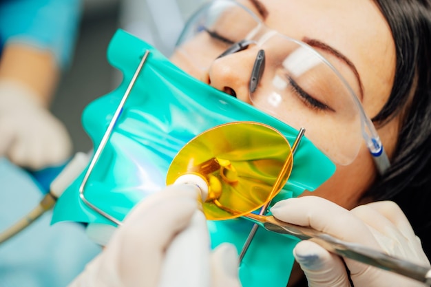 Female patient in medical glasses having dental check up in stomatology office Dentist's hands in white gloves working with instruments in woman's mouth Closeup