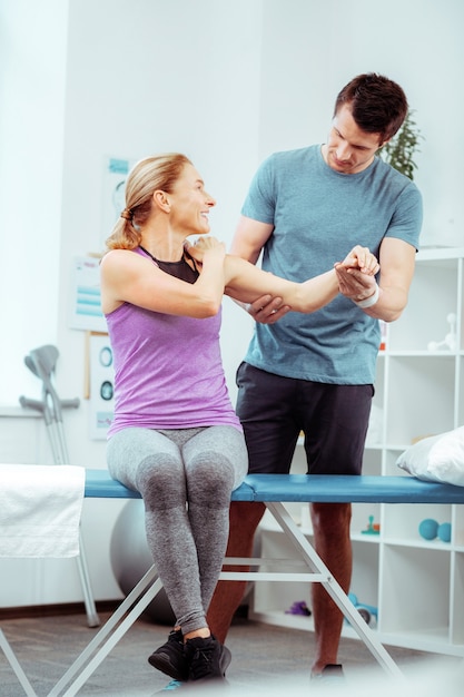 Female patient. Positive joyful woman pointing at her shoulder while speaking to her doctor